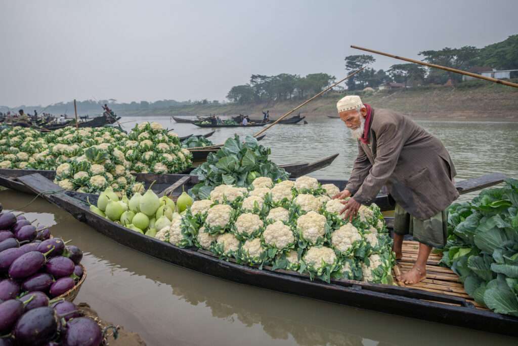 Mann verkauft Gemüse auf einem Boot auf einem schwimmenden Markt in Bangladesch
