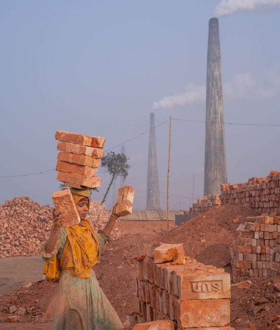 Frau trägt mehrere Ziegelsteine auf dem Kopf durch eine Ziegelfabrik in Bangladesch
